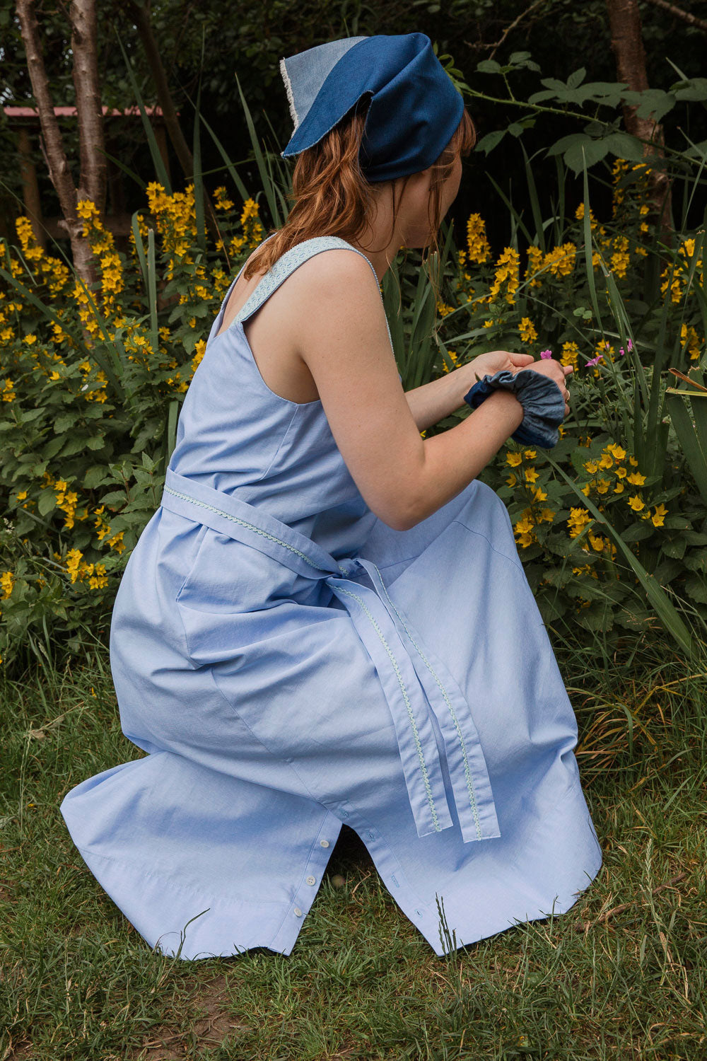 Maya Cami Dress in pale blue recycled cotton, three-quarter view, model in a woodland wildflower setting. By Saywood. Made in London.