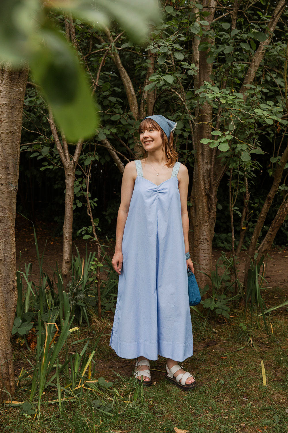 Maya Cami Dress in pale blue recycled cotton, worn without belt, full length, smiling model in a woodland setting. By Saywood. Made in London.