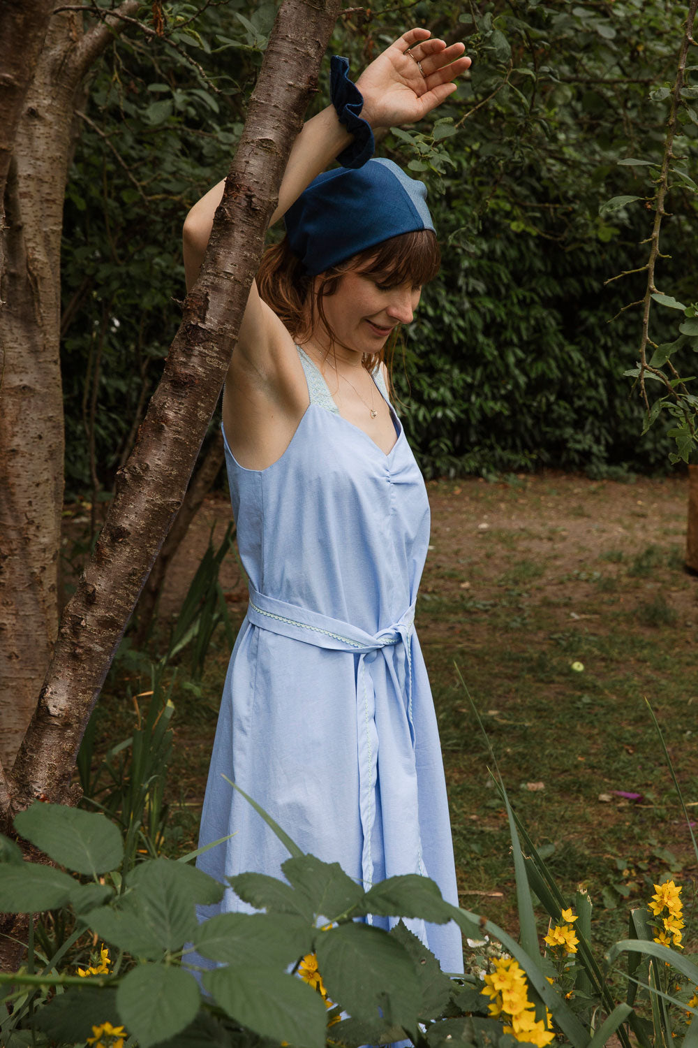 Maya Cami Dress in pale blue recycled cotton, styled with detachable tie belt in a garden setting. By Saywood. Made in London.