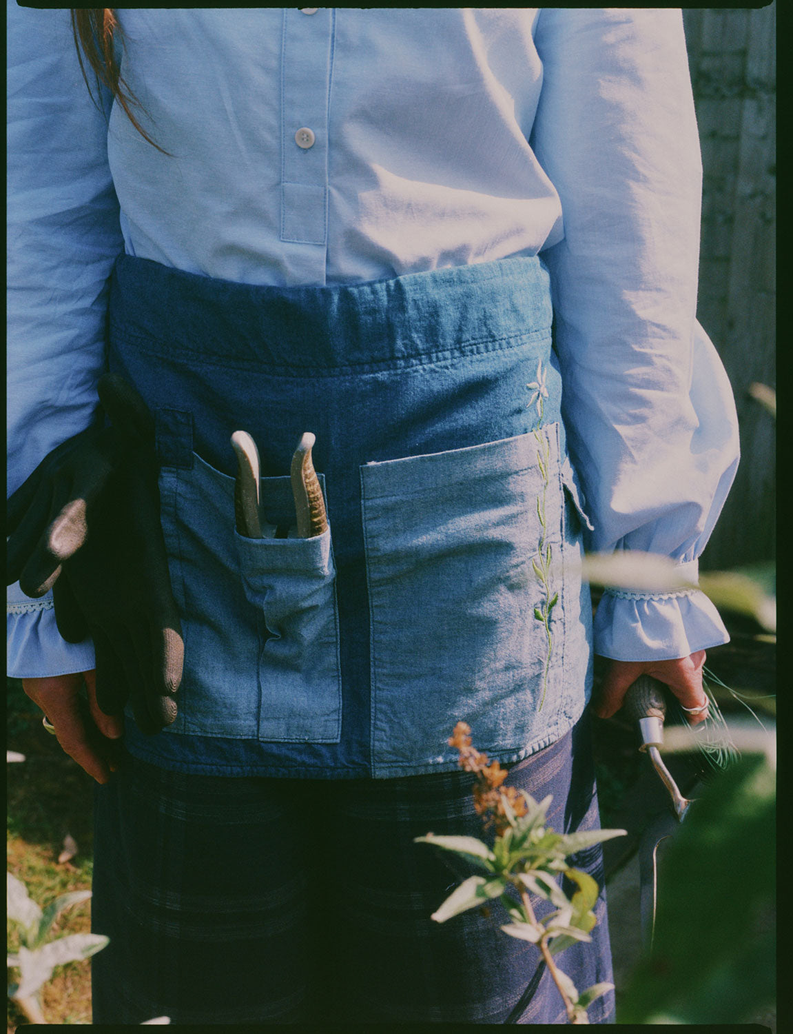 Close-up of Japanese denim gardener's apron with embroidered flower and secateurs in tool pocket, by Saywood
