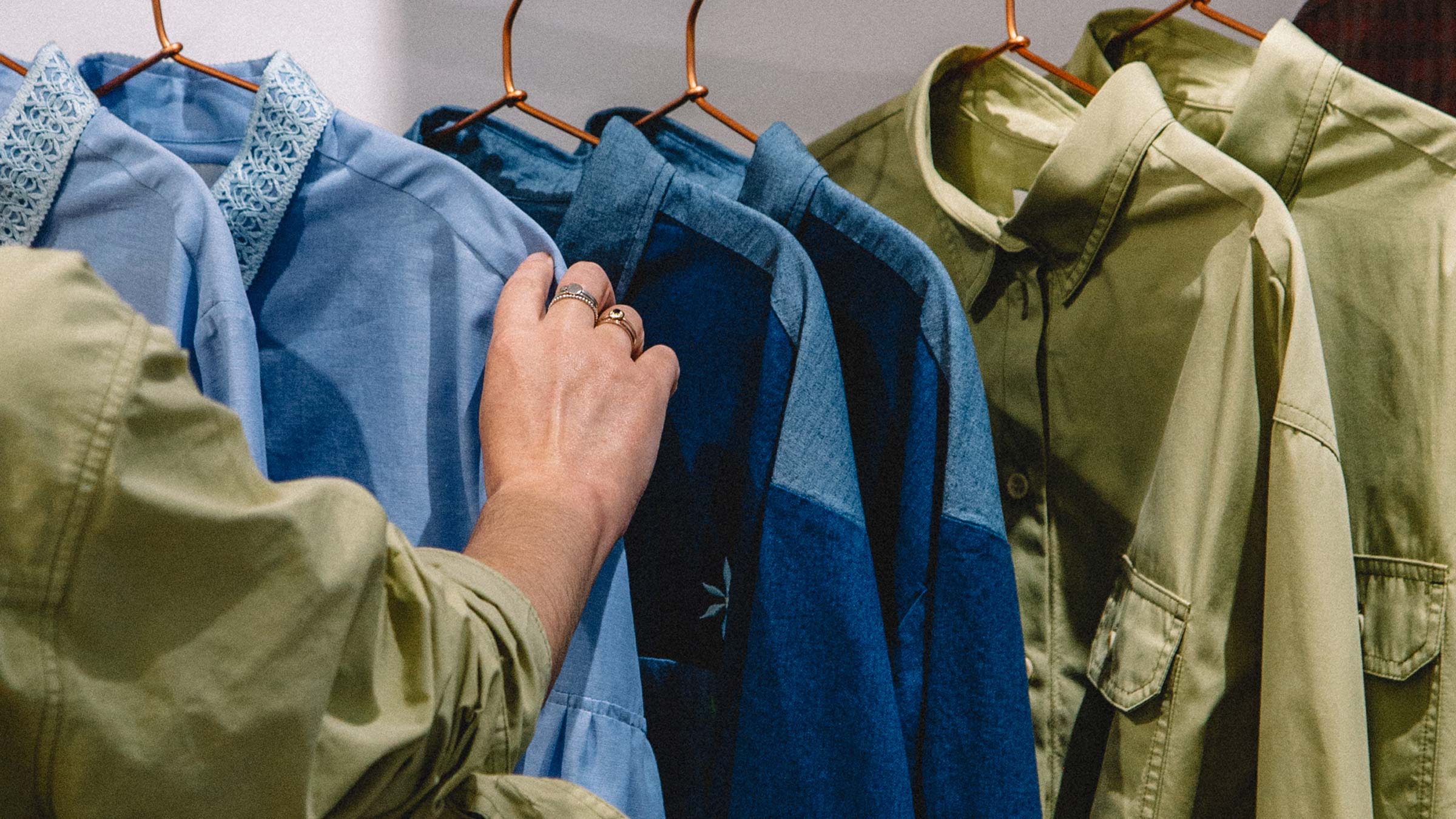 Browsing a rail of natural fibre shirts in blue and olive — sustainable materials used by Saywood