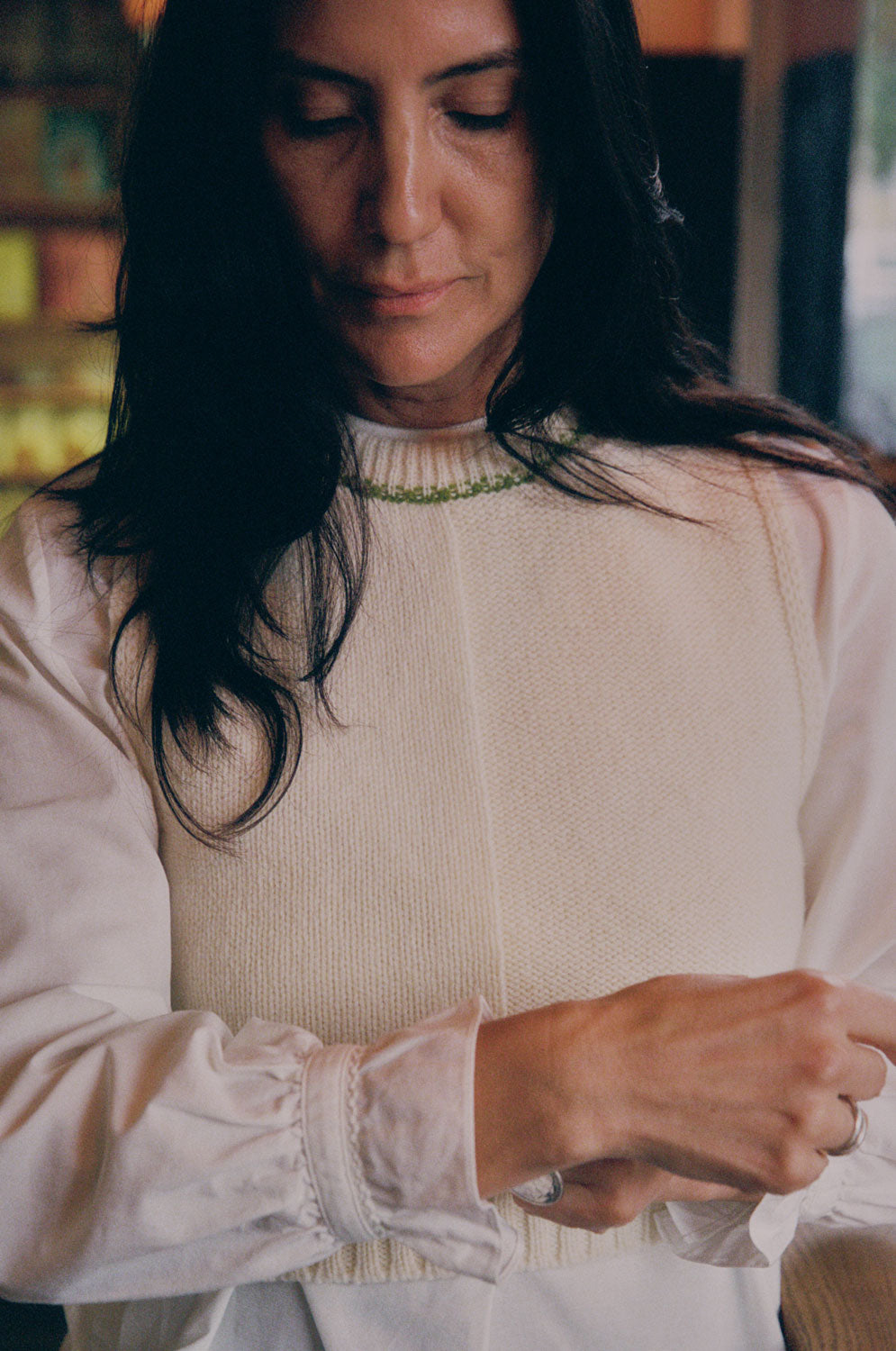 Close-up detail of cream Ada Sweater Vest showing textured half-purl, half-jersey lambswool knit and moss green contrast stitching at neckline.