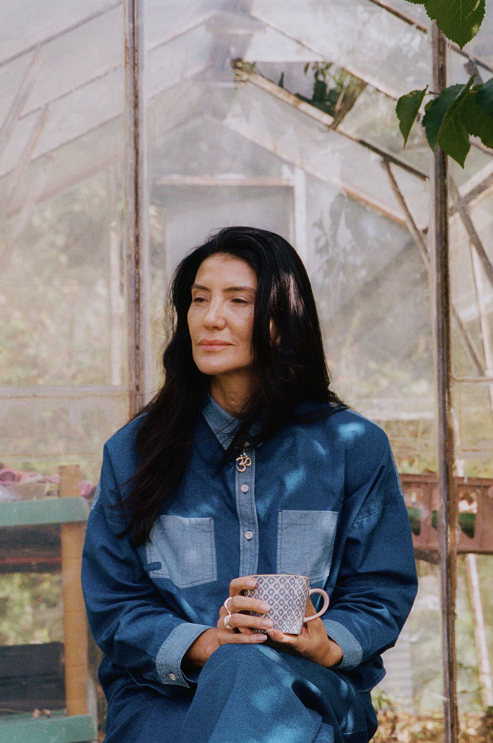 Woman with tea at greenhouse wearing Lela indigo Japanese denim patchwork shirt and Amelia trousers