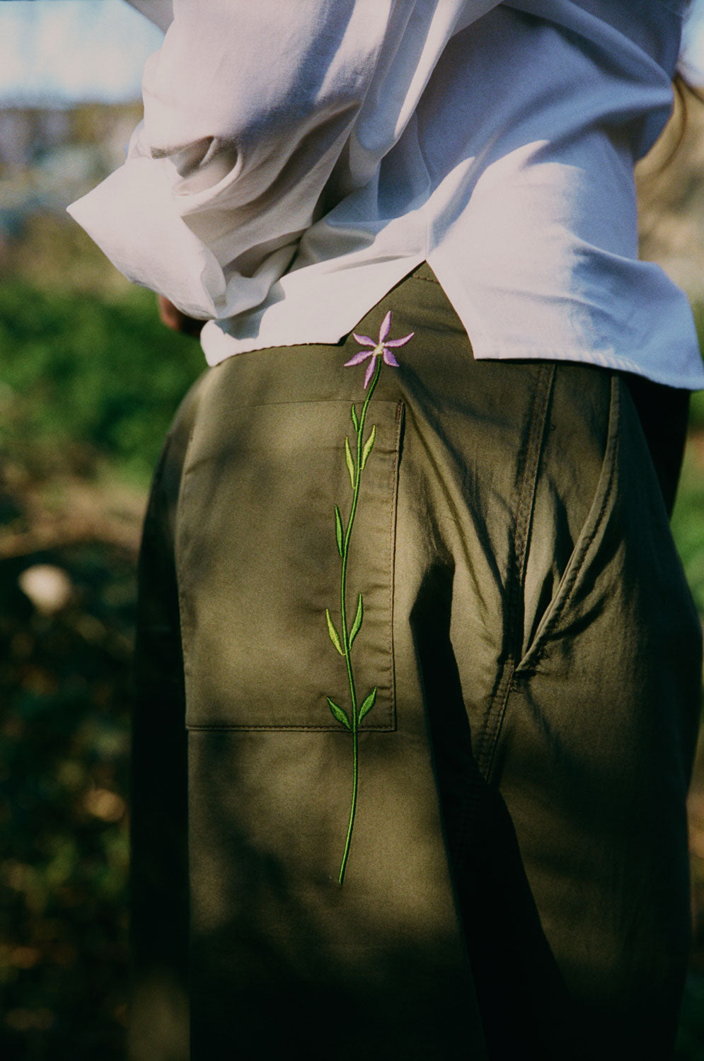 Close-up detail of Amelia trousers back pocket with signature embroidered flower, khaki deadstock cotton with white Lela shirt by Saywood