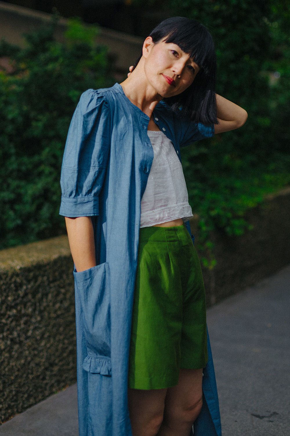 Rosa light wash denim shirtdress styled open over white vest and green shorts