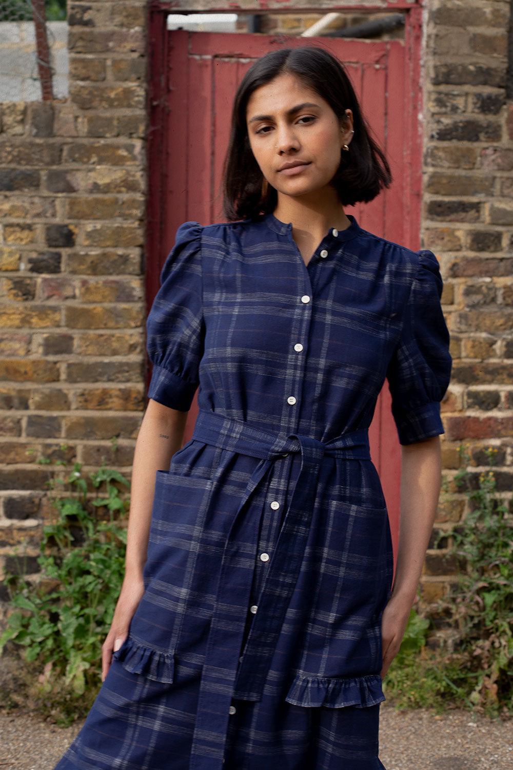 Close-up detail of Rosa shirtdress puff sleeves and ruffle pocket trim in navy check surplus cotton by Saywood