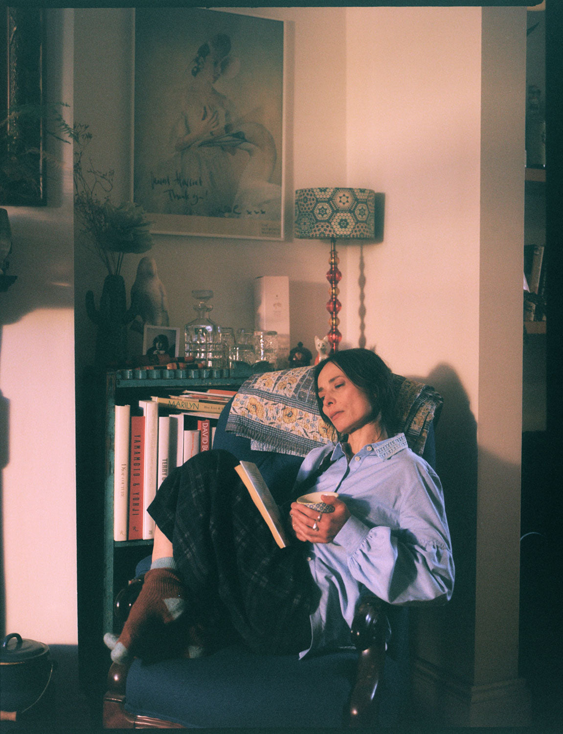 Woman in Edi pale blue shirt with Amelia navy check trousers in cosy reading scene