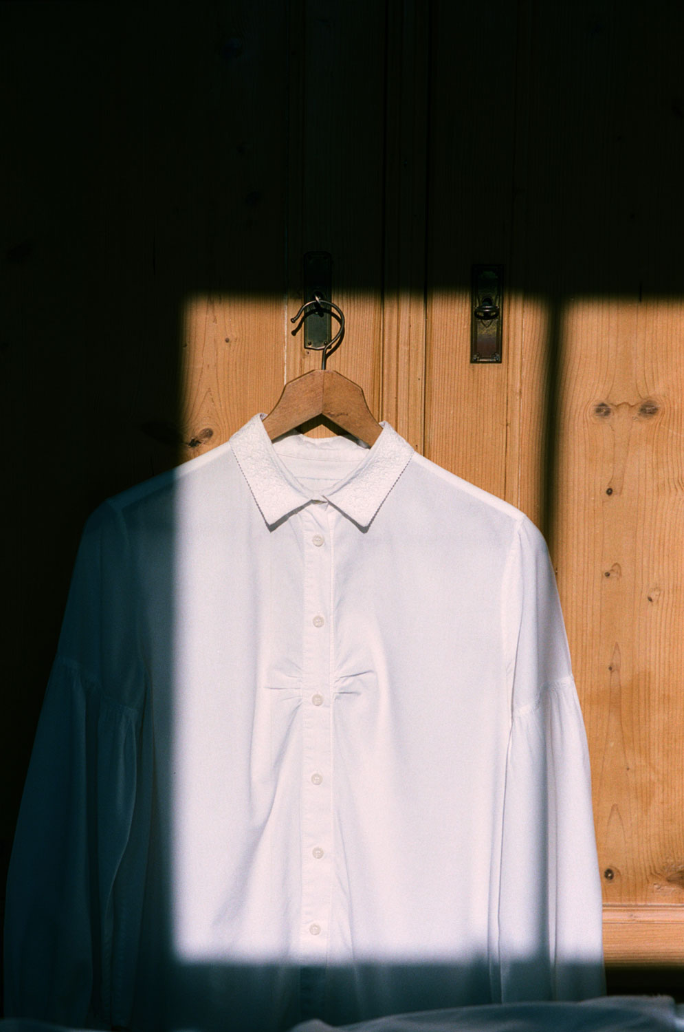 Edi white shirt with lace collar hanging on wardrobe in natural sunlight showing gathered bust